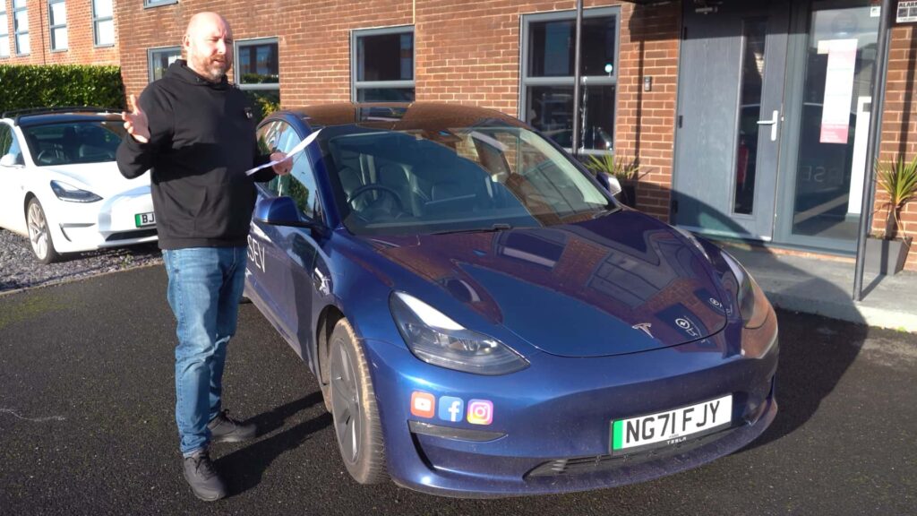 Mand står ved siden af en blå Tesla Model 3 parkeret foran en bygning