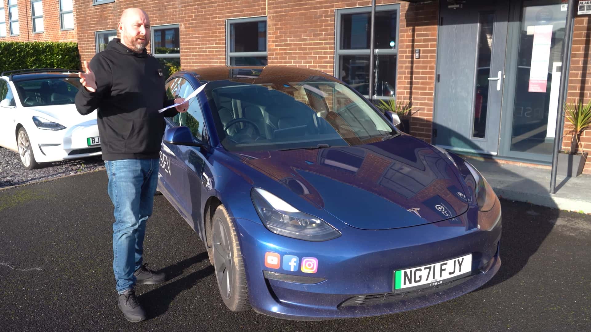 Mand står ved siden af en blå Tesla Model 3 parkeret foran en bygning