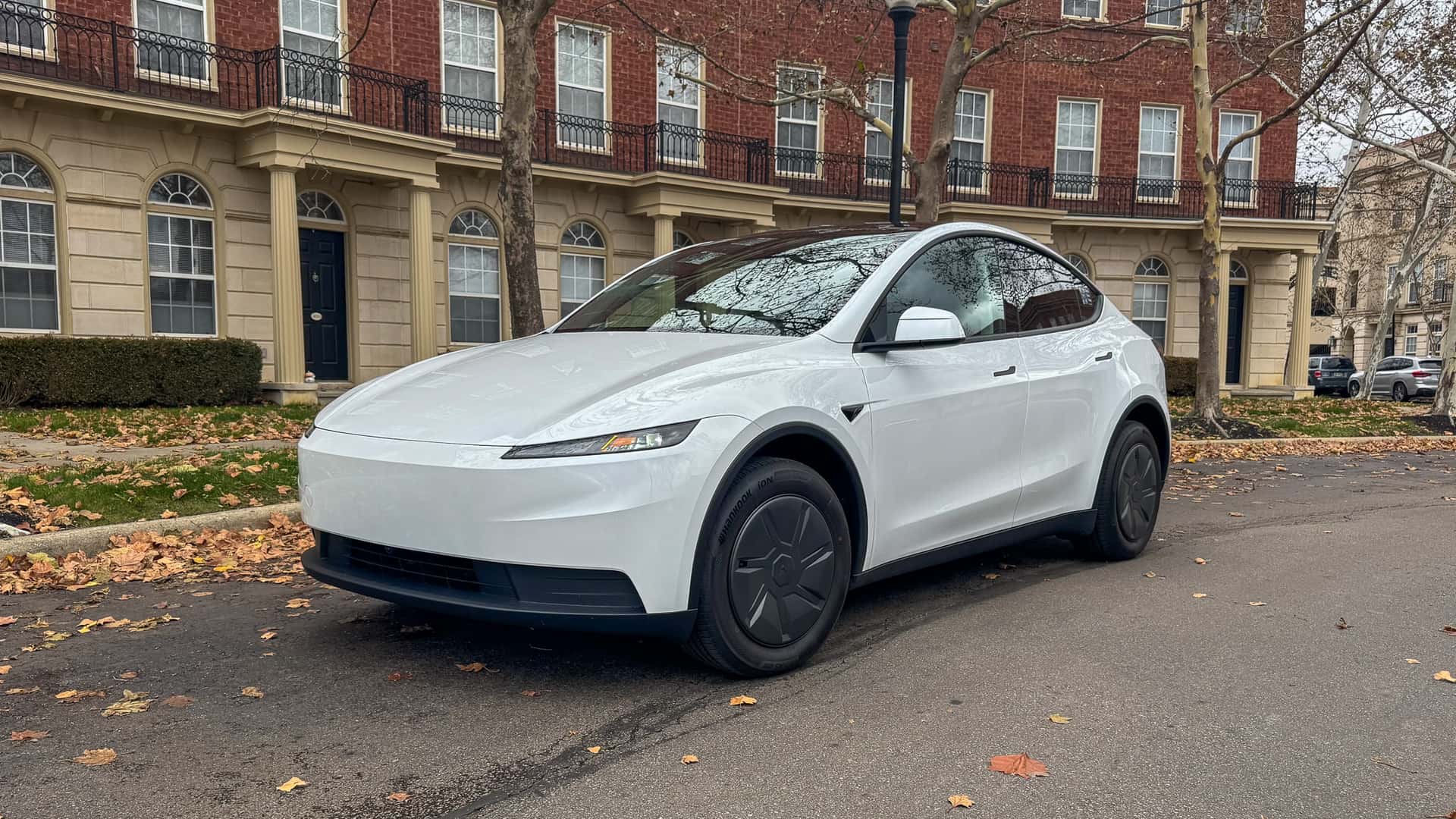 Hvid Tesla elbil parkeret foran en murstensbygning med søjler og vinduer