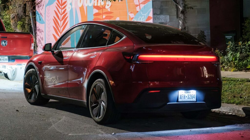 Rød Tesla elbil parket på en byvej om natten med farverig vægudsmykning i baggrunden