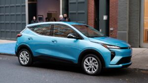 Lyseblå elektrisk bil parkeret på en gade foran en bygning.