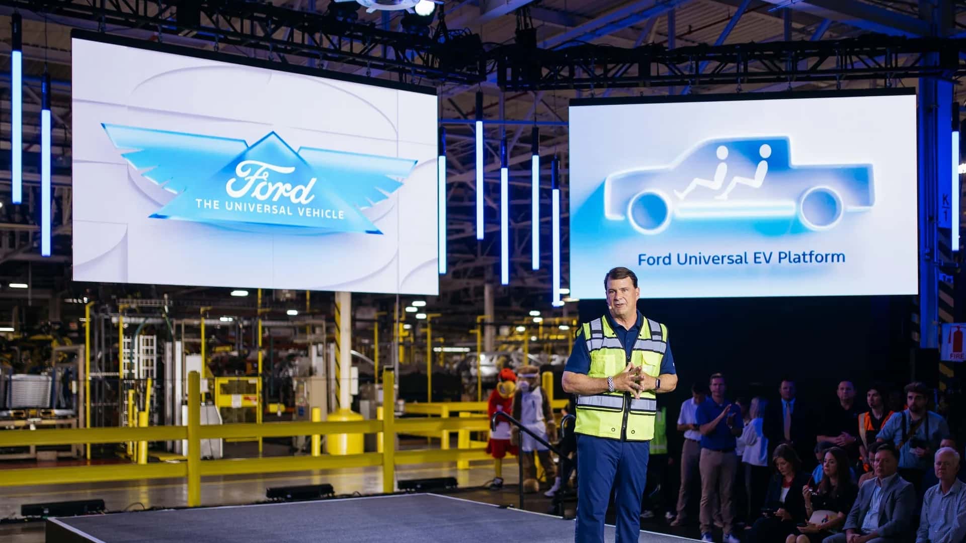En mand ved en præsentation af Ford Universal EV Platform på en messe, omgivet af publikum.