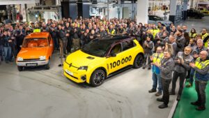 Mennesker samlet omkring gule og orange Renault biler i en fabrikshal, fejrer produktion af 100.000 køretøjer