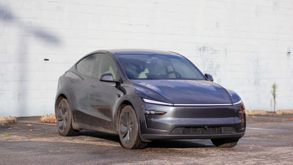 Mørkegrå Tesla Model Y parkeret ved en hvid mur