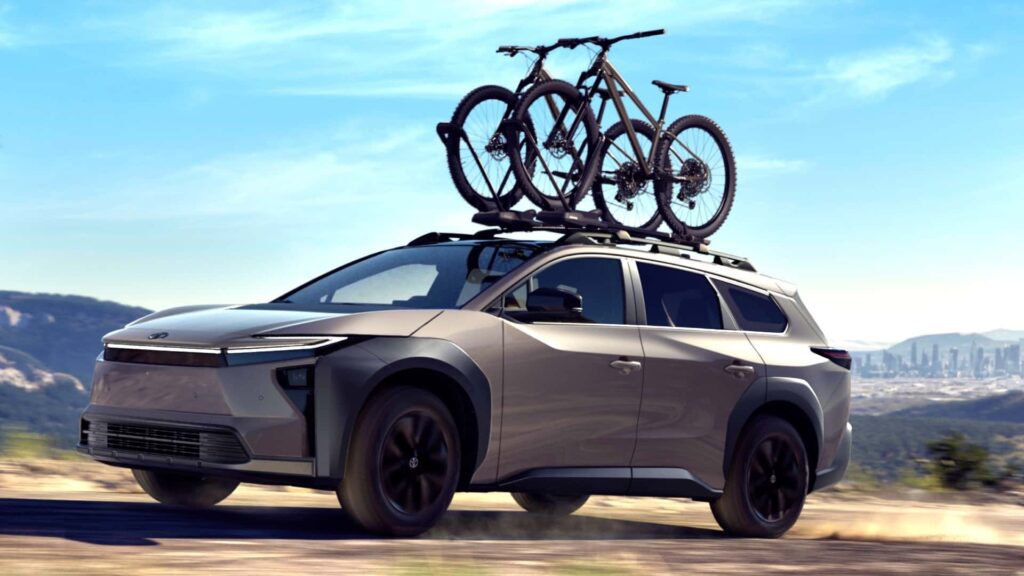 Moderne elbil med cykler på taget, kørende i åbent landskab
