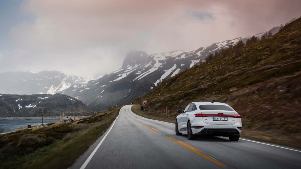 Hvid Audi elbil kører på en naturskøn bjergvej under skyet himmel