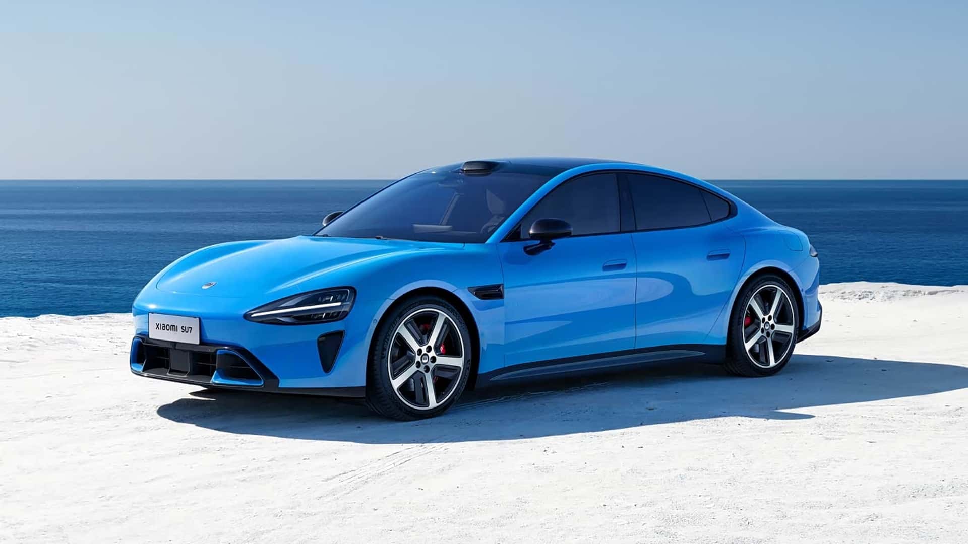 Blå elbil parkeret ved havet under en klar himmel