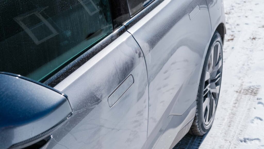 Nærbillede af sidepanelet på en Tesla elbil, der står parkeret i sneen