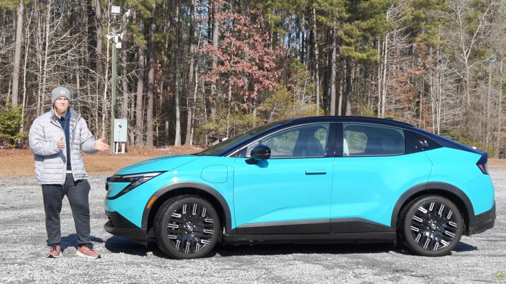 Person står ved siden af en elektrisk bil i lyseblå farve i en skov.