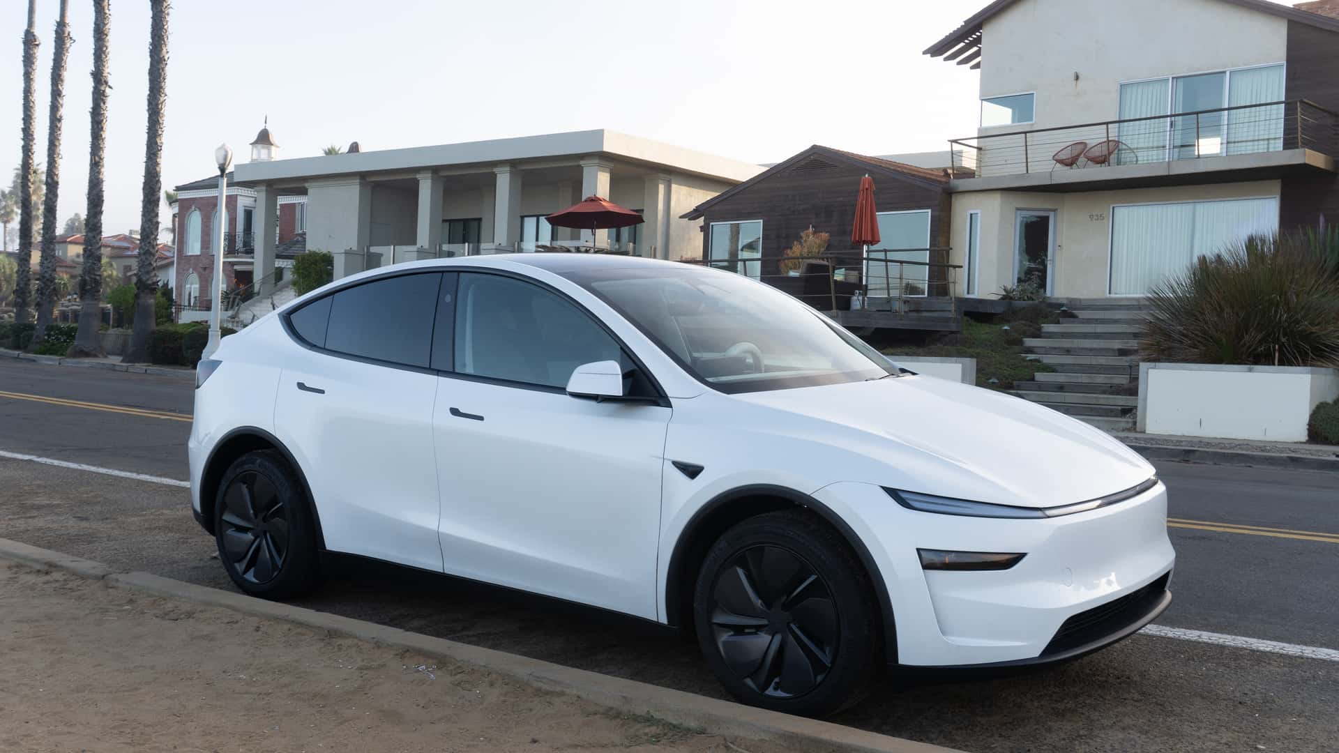 Hvid Tesla elbil parkeret foran moderne huse ved vejen