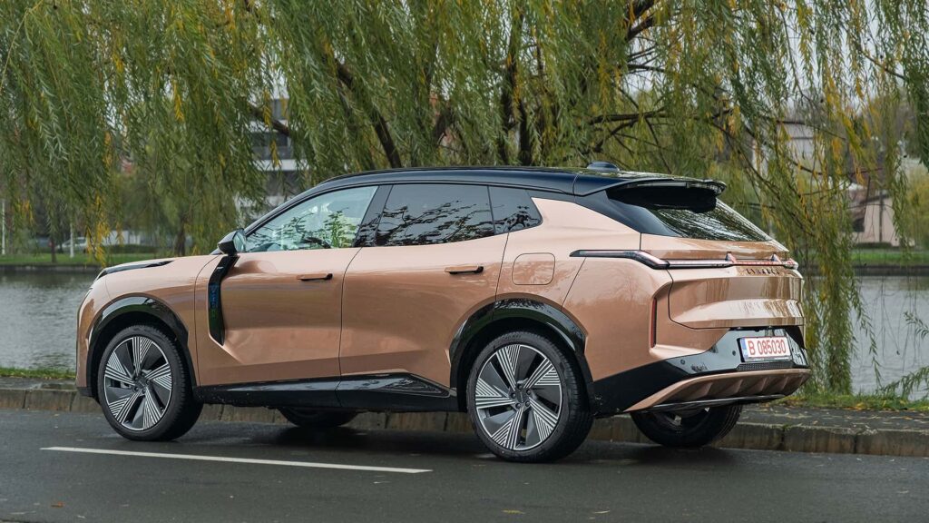 Brun elektrisk SUV parkeret ved en flod, omgivet af grønne træer