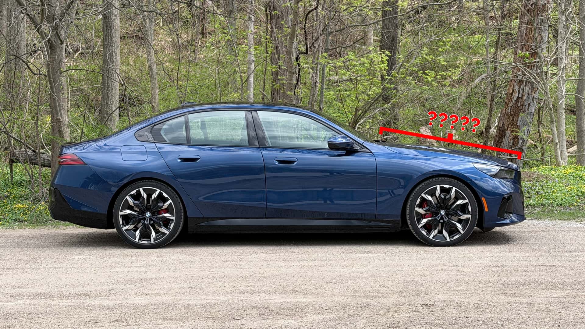 Blå sedanbil parkeret på en skovvej med rød markering på motorhjelmen