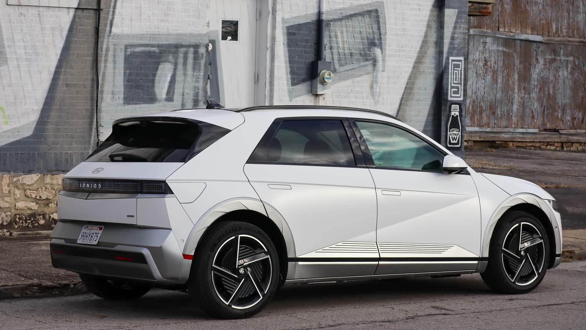 Hvid elektrisk bil parkeret foran en væg med gadekunst