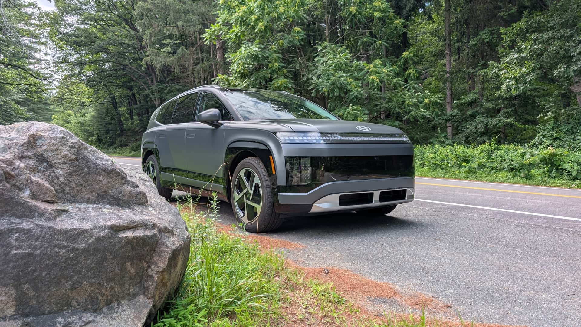 Elektrisk SUV parkeret ved landet vej omgivet af skov