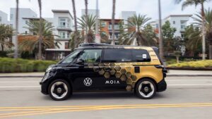 Volkswagen MOIA autonom minibus på vej langs en gade med moderne bygninger og palmer i baggrunden