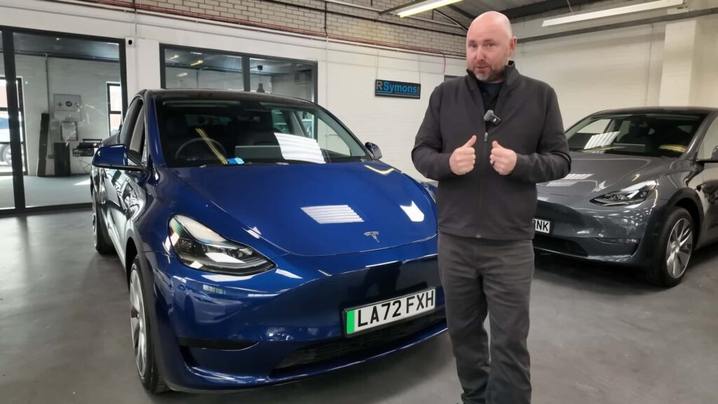 Mand står foran en blå Tesla i en garage