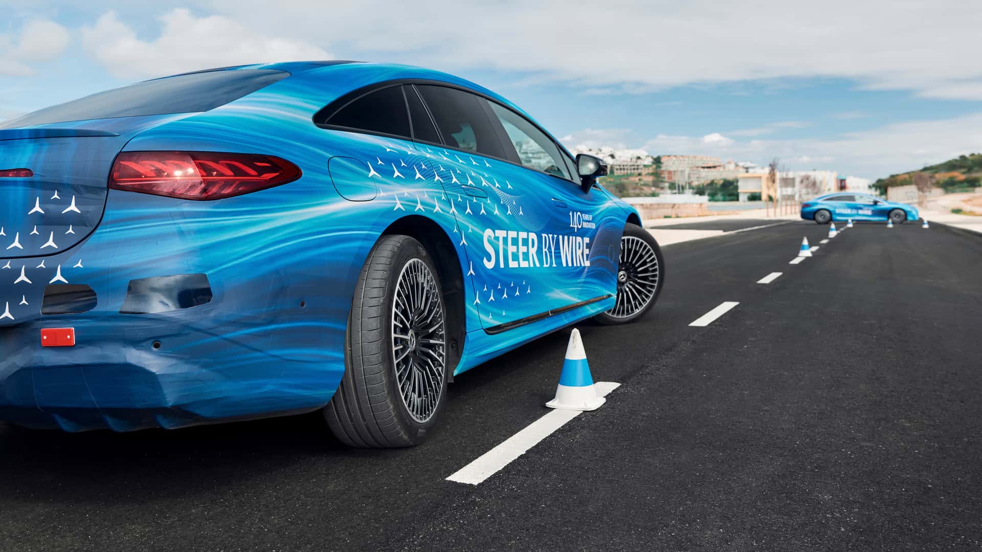 Blå elektrisk bil med skiltet 'Steer by Wire' kører på testbane