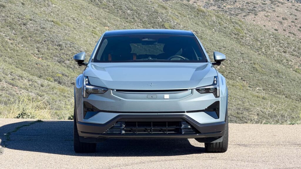 Fronten af en innovativ elbil parkeret på en naturskøn bakke med græs og blå himmel i baggrunden