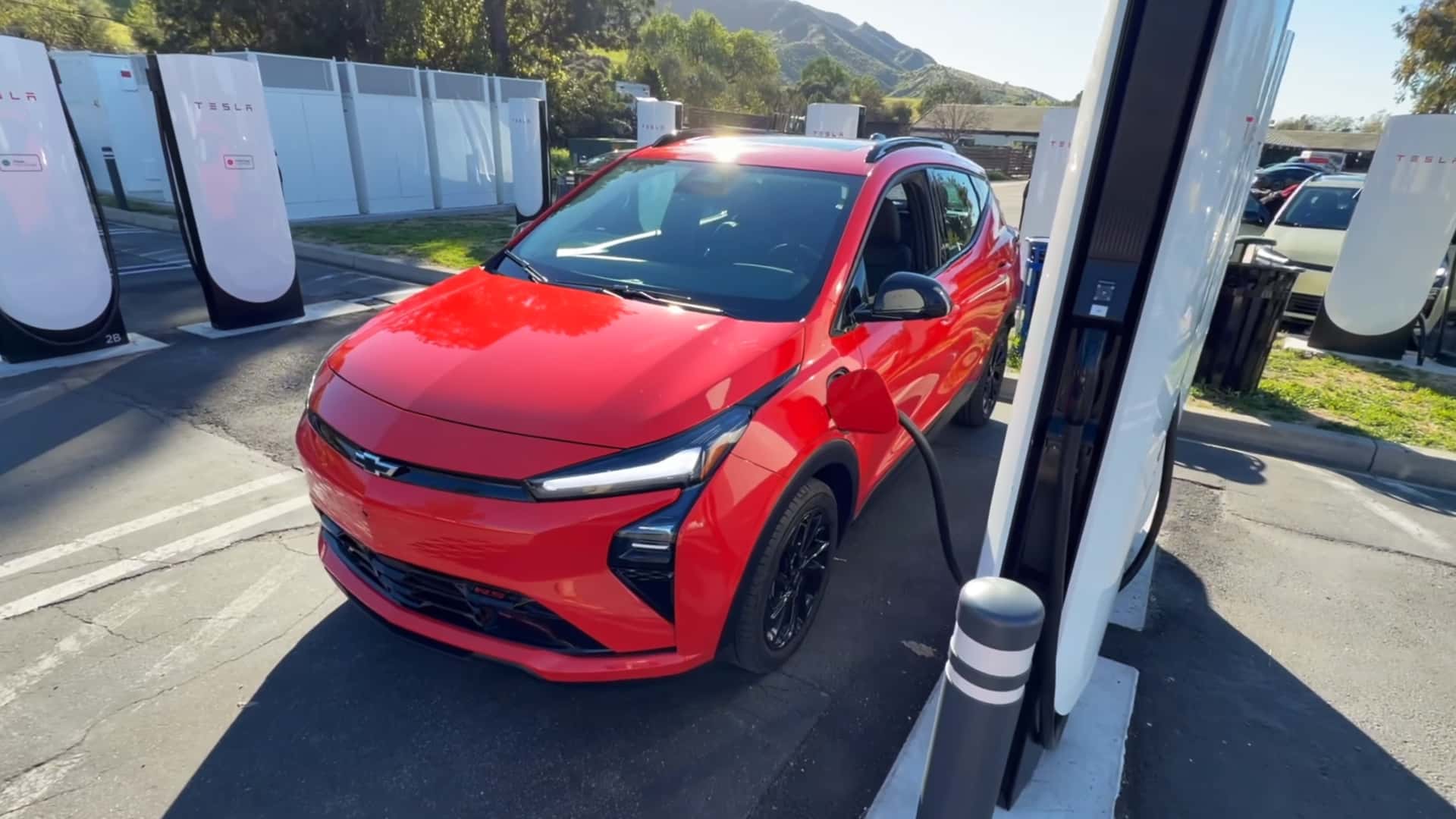Rød elbil oplades ved Tesla-ladestation i et solrigt område