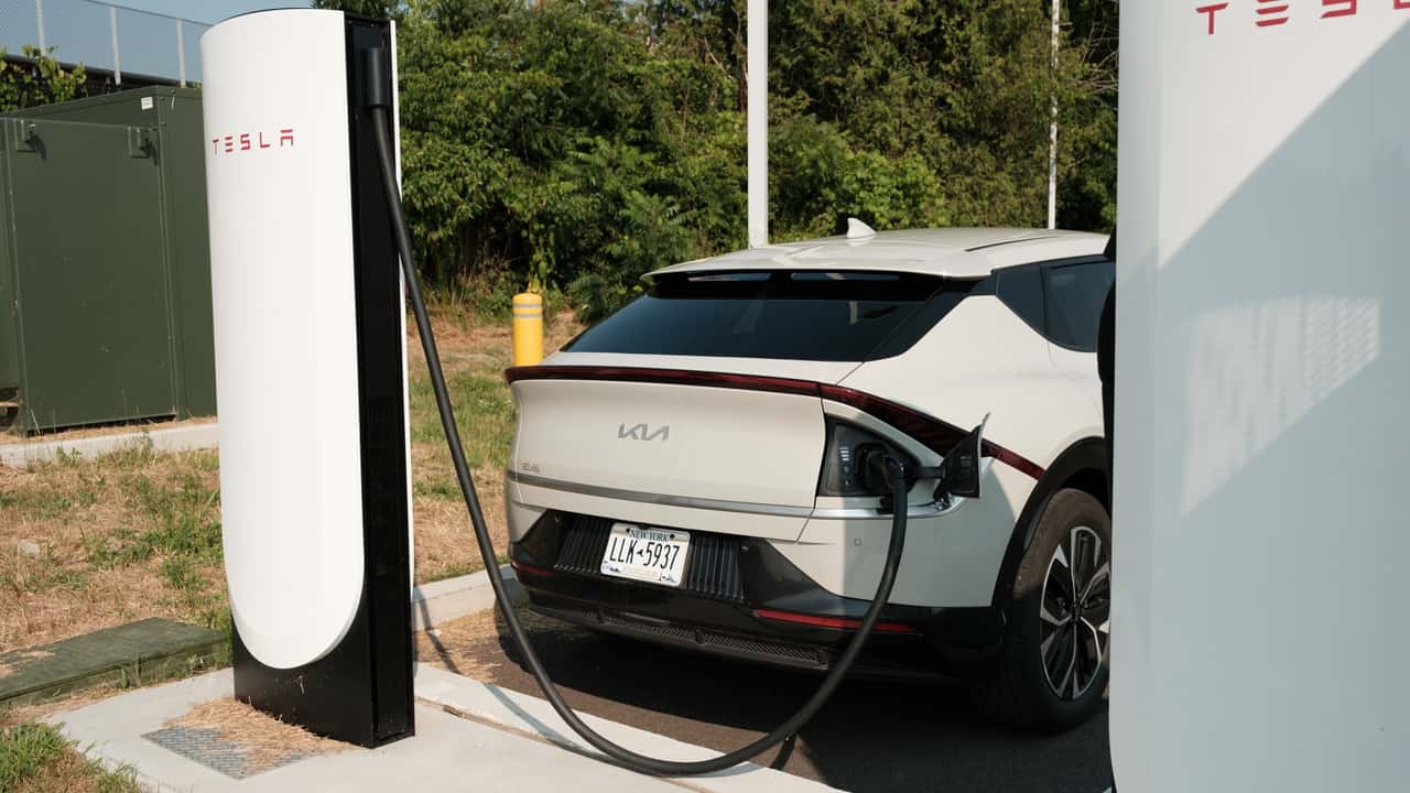 Elbil oplader ved en Tesla ladestation i grønne omgivelser
