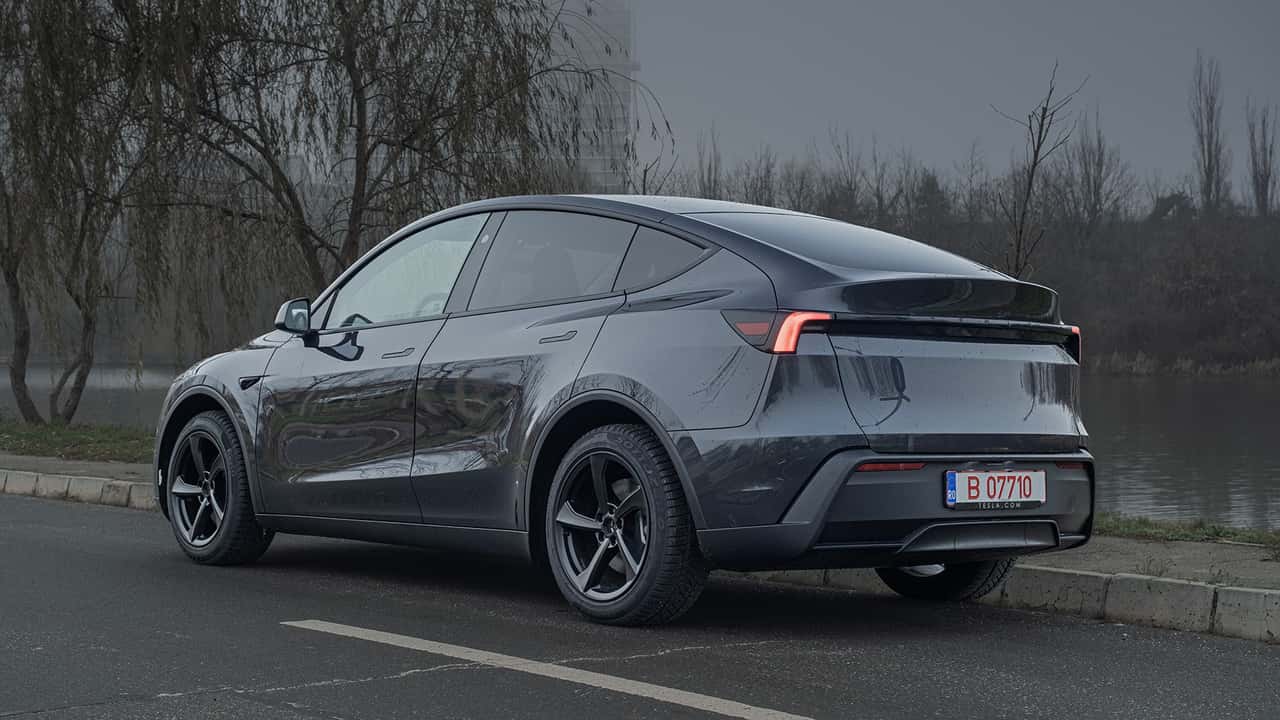 Mørkegrå Tesla elbil parkeret ved siden af en sø på en overskyet dag
