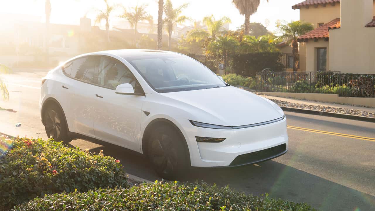 Hvid Tesla elbil parkeret i solen på en stille vej omgivet af palmer