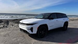 Hvid SUV parkeret på en strand med havet i baggrunden
