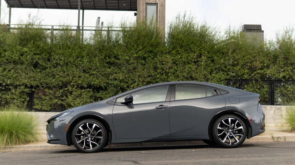 Toyota-logo, parkeret grå sedan ved hæk