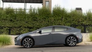 Toyota-logo, parkeret grå sedan ved hæk