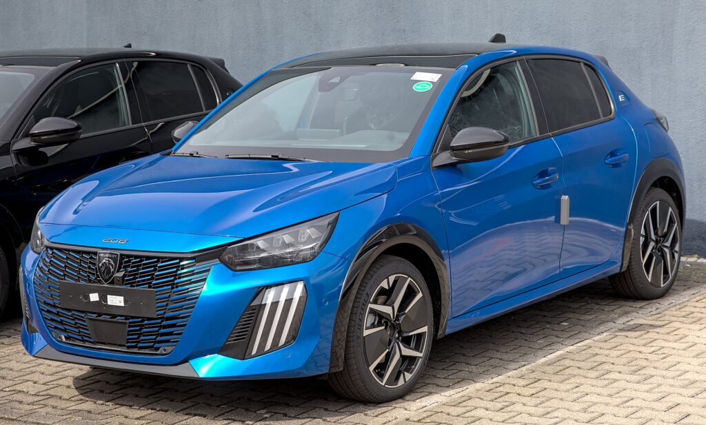 Blå Peugeot E-208 efter faceliftet, parkeret på en forhandlers plads