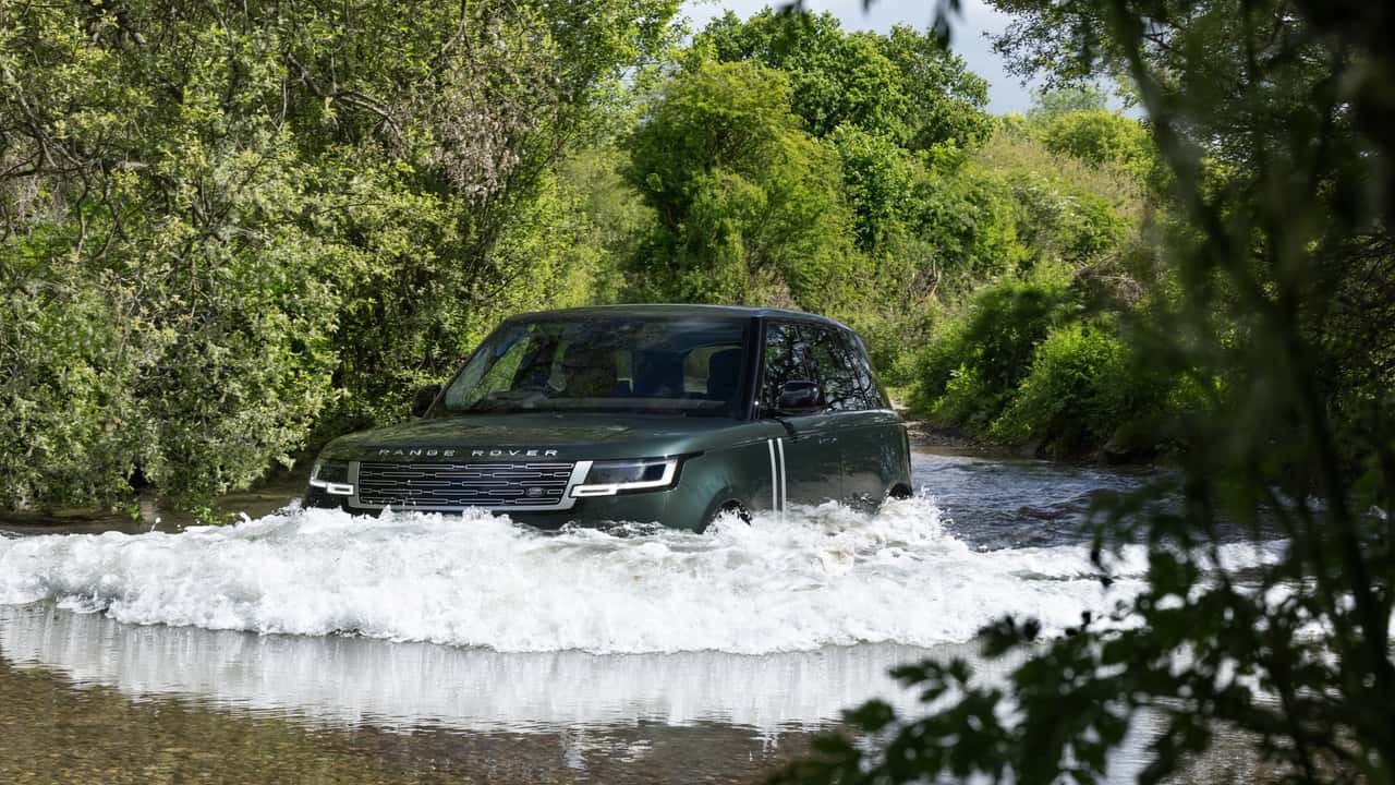Range Rover kører gennem vand i skovområde