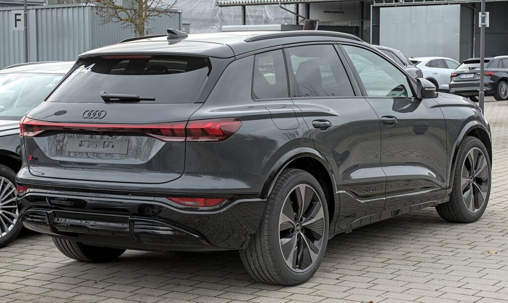 Mørkegrå Audi Q6 e-tron set skråt bagfra på en brostensbelagt parkeringsplads