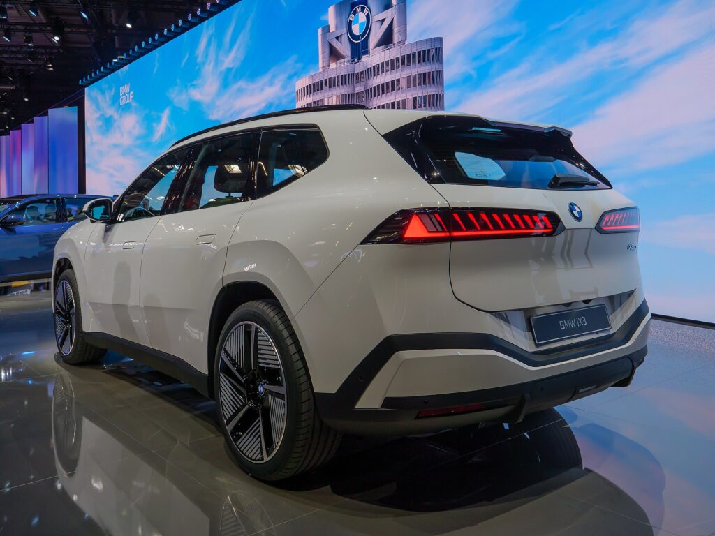 Hvid BMW iX3 af den nye generation set skråt bagfra på en udstilling
