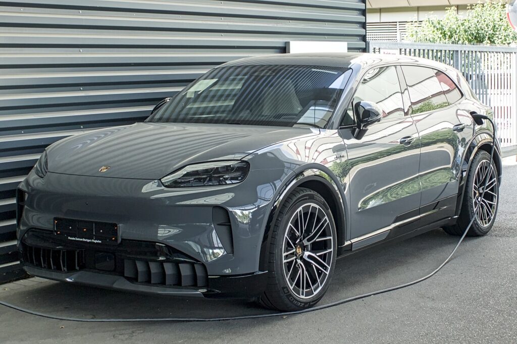 Grå Porsche Cayenne Electric parkeret foran en metalvæg med ladekablet sat i