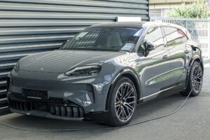 Grå Porsche Cayenne Electric parkeret foran en metalvæg med ladekablet sat i