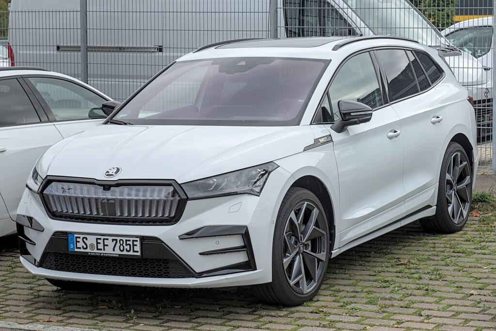 Hvid Škoda Enyaq RS med oplyst grill parkeret på en græsarmeret parkeringsplads