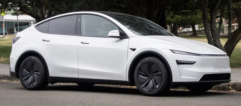 Hvid Tesla Model Y af den nye generation set skråt forfra ved en vej med træer