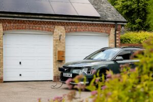 Grøn elbil tilsluttet ladeboks foran et hus med solceller på taget