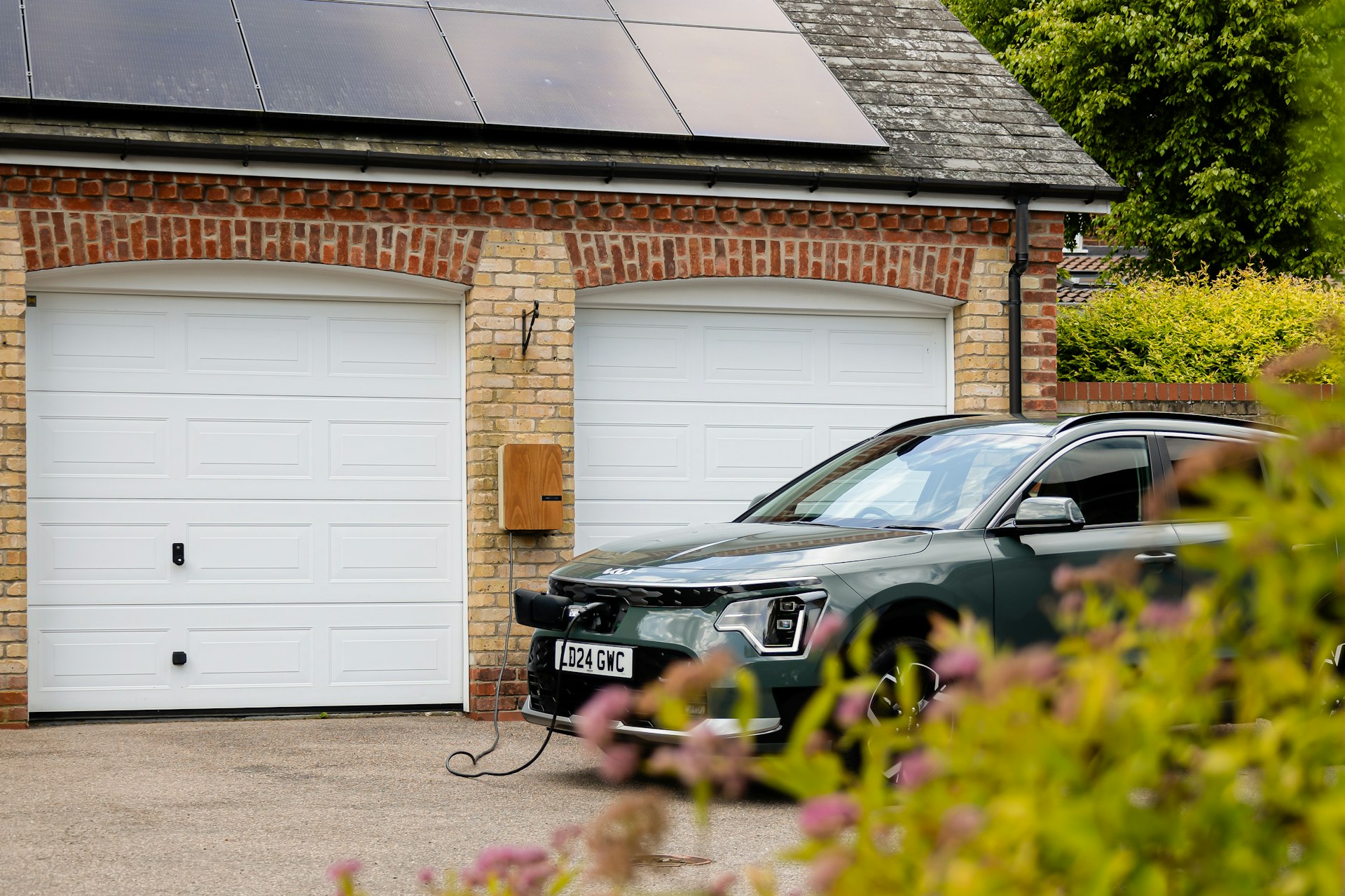 Grøn elbil tilsluttet ladeboks foran et hus med solceller på taget