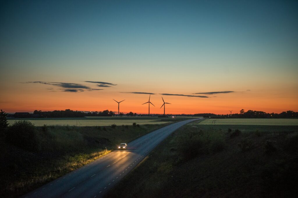 Bil kører ad en landevej i solnedgang med vindmøller i horisonten