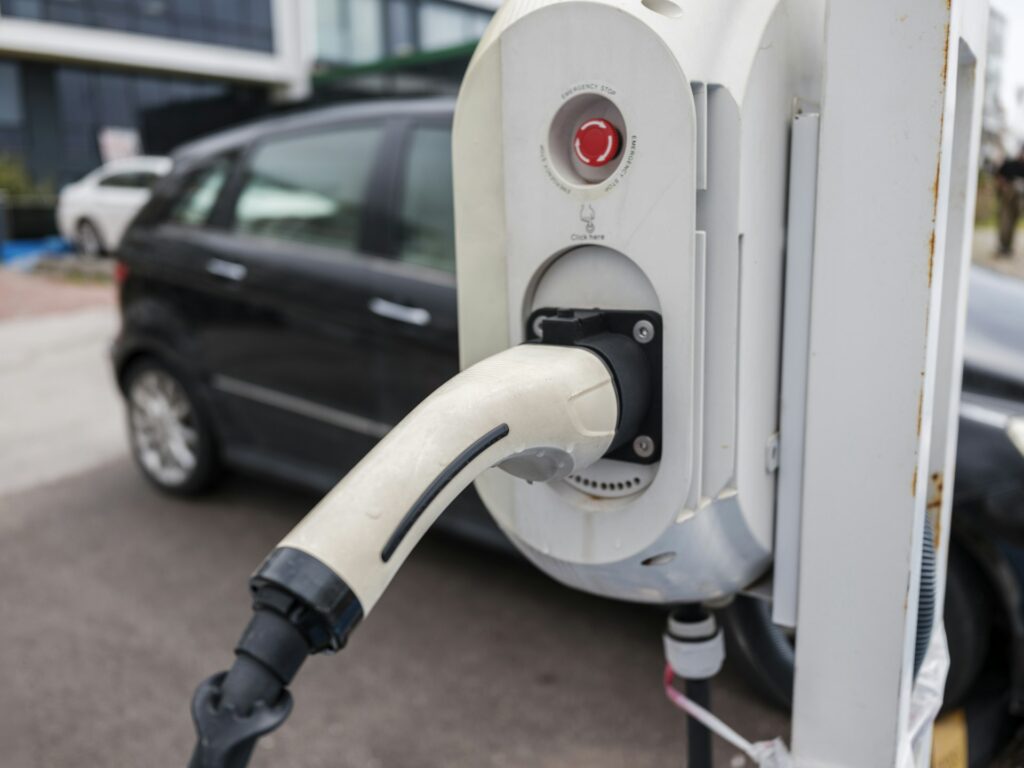 Ladestik sat i en offentlig ladestander med en bil parkeret bagved